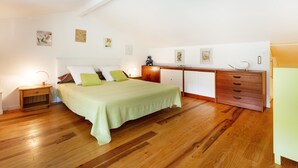 Een slaapkamer met een bed, houten vloer, nachtkastjes, een dressoir en wanddecoratie.