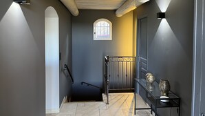 A narrow hallway with a wooden ceiling, a small window, a metal railing, and a table with decorative items. - Villa Théia (Flayosc)