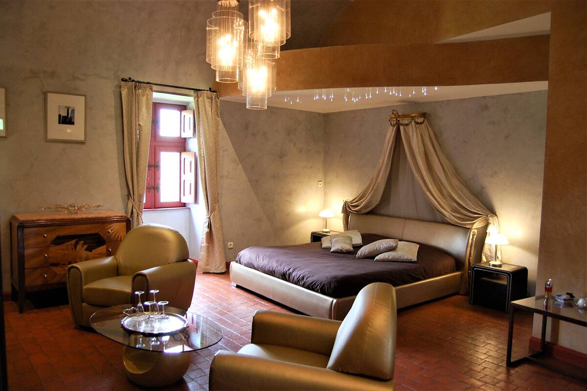 Ein Schlafzimmer mit einem Bett, zwei Stühlen, einem kleinen Tisch und einem Nachttisch mit einer Lampe.