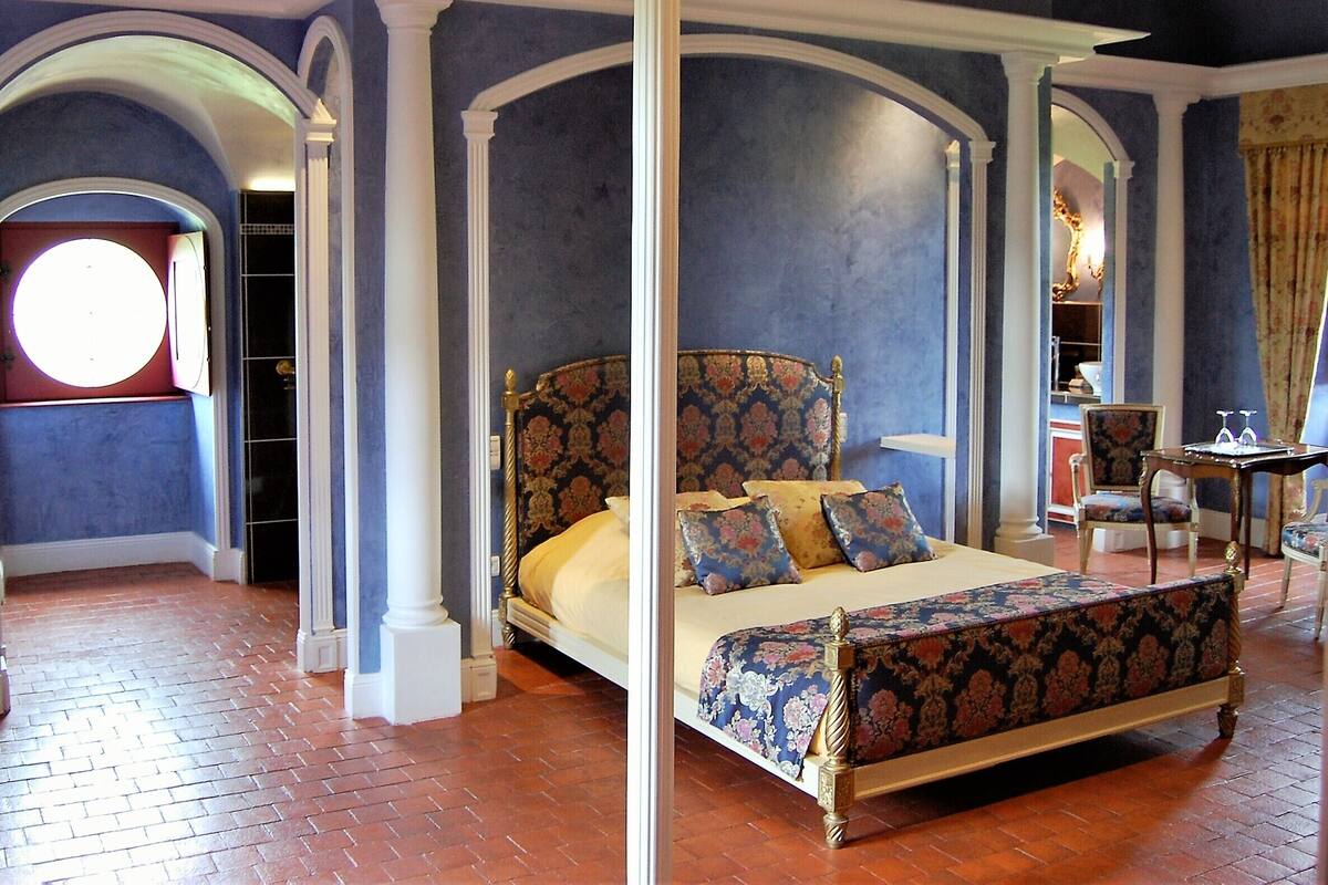 Ein Himmelbett mit floralem Kopfteil, einem Rundfenster und einem Boden aus Ziegelsteinen.
