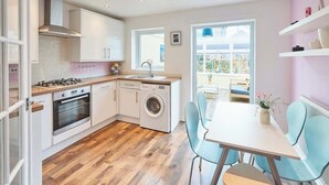 Een moderne keuken met een wasmachine, een eethoek met stoelen en een uitzicht door een raam.