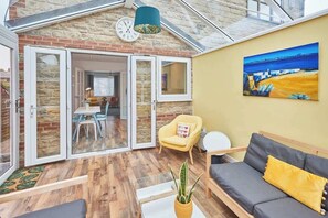 Une pièce chaleureuse avec un plancher en bois, un canapé, un fauteuil jaune et un tableau accroché au mur.