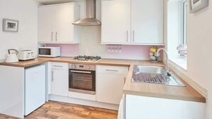 Een kleine keuken met witte kastjes, een magnetron, een fornuis en een spoelbak.