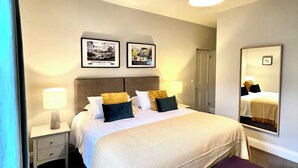 Habitación de hotel ordenada con una cama grande, mesitas de noche con lámparas, un espejo y dos cuadros en la pared.