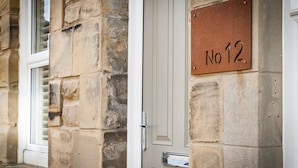 A stone building with a door labeled "No 12" and a window with blinds.