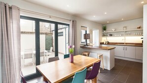 Una cocina moderna con una mesa de madera y sillas coloridas, una pequeña isla con un lavaplatos y vistas al exterior a través de ventanas amplias.