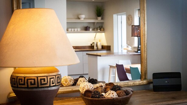 Una lámpara con un diseño geométrico sobre una mesa, un cuenco con objetos decorativos y una cocina al fondo.