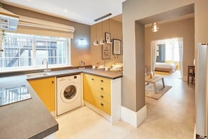 A compact kitchen with a washing machine, a dining area with a table and chairs, and a view of the outside through a window.