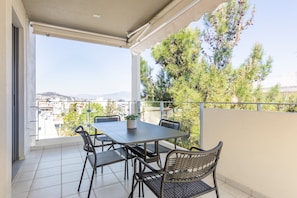 A balcony with a table and chairs, a potted plant, and a view of a cityscape and mountains.