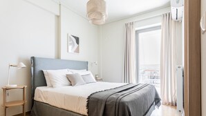 Une chambre à coucher moderne avec un lit, des tables de chevet, un luminaire suspendu et une fenêtre avec des rideaux.