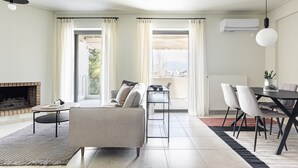 Un salon moderne avec une cheminée, un canapé, une table à manger avec des chaises et une vue dégagée grâce à de grandes fenêtres.