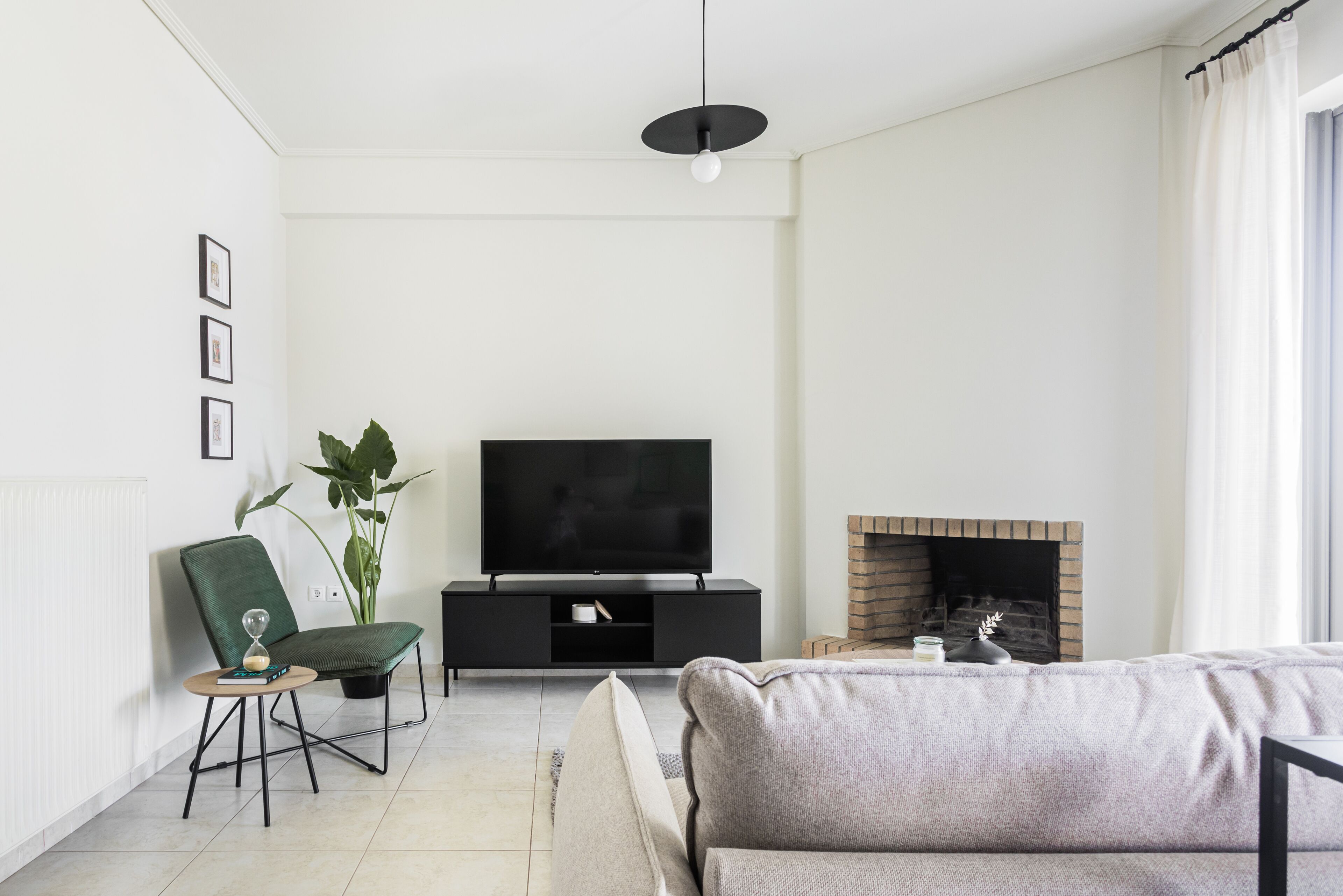 A modern living room with a flat-screen TV, a fireplace, a green chair, and a sofa.