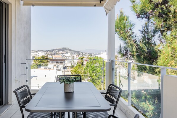 A balcony with a table and chairs, overlooking a cityscape with buildings and trees.