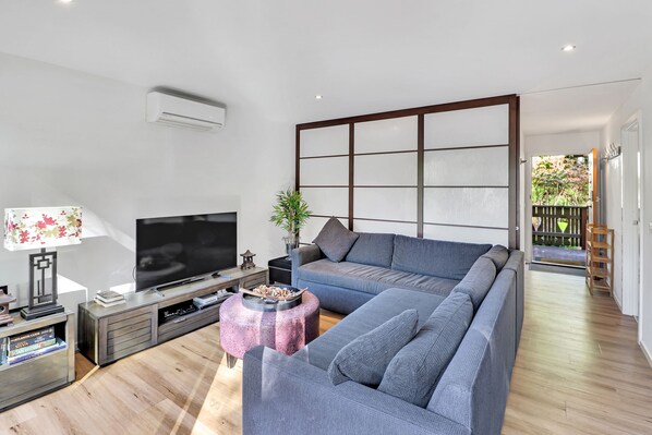 Una sala de estar moderna con un sofá seccional, un televisor de pantalla plana, una mesa de centro y piso de madera.