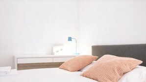 Una cama bien hecha con dos almohadas, una mesita de noche con lámpara y un cabecero gris.