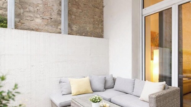 Una sala de estar moderna con un sofá modular gris, una mesita con una planta y un ventanal con vistas a un edificio.