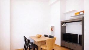 Una sala de estar moderna con una mesa de comedor de madera, dos sillas, un mueble de televisión con televisor de pantalla plana y un estante con objetos.