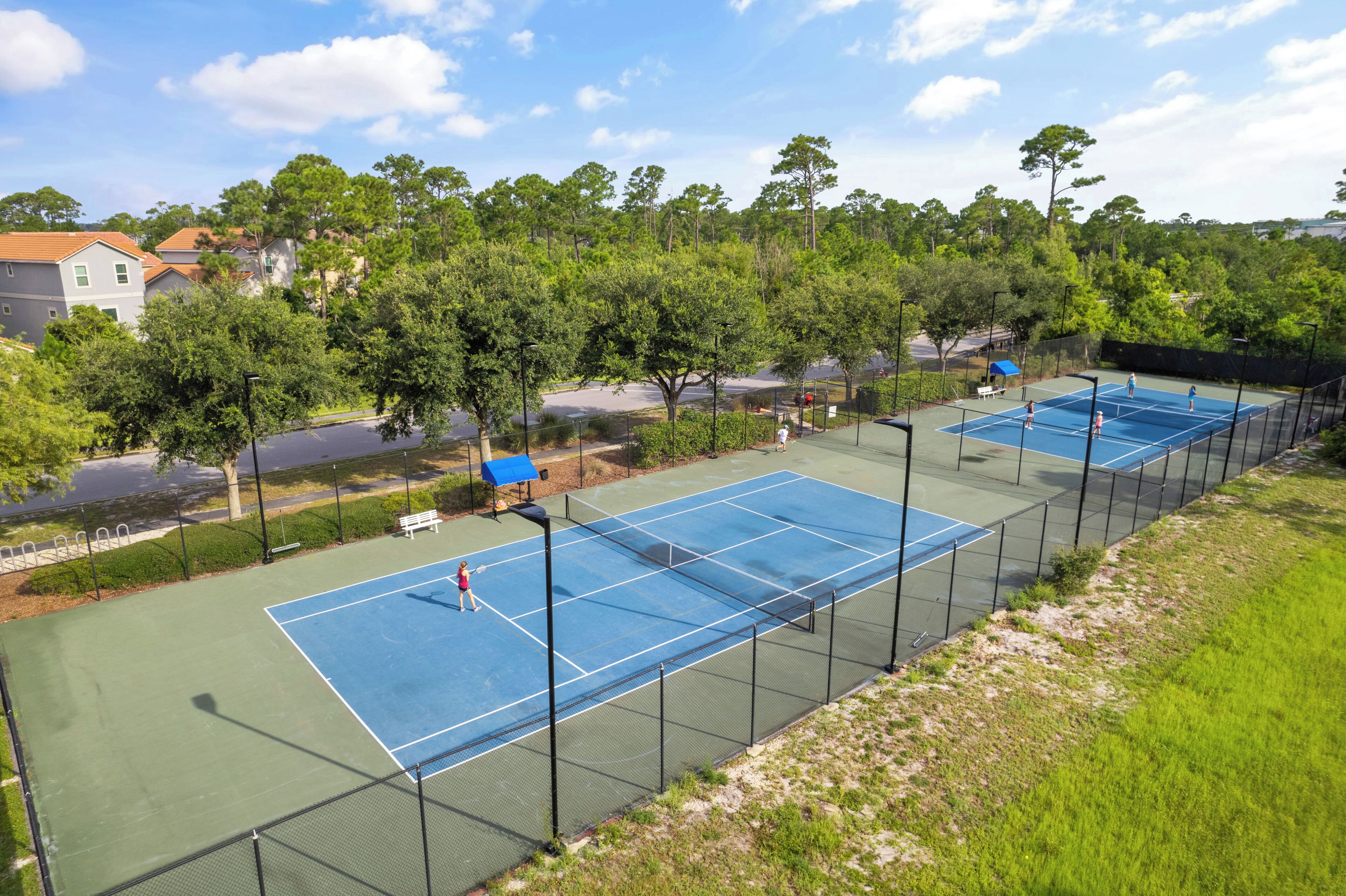 Un court de tennis avec un filet, entouré d’arbres et d’une clôture.