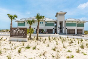 Un club de plage avec un panneau indicateur, des palmiers et un bâtiment aux couleurs vert et blanc.