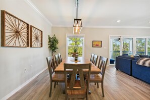 Un coin repas avec une table et des chaises en bois, un luminaire suspendu et une vue sur l’extérieur grâce à une grande fenêtre.