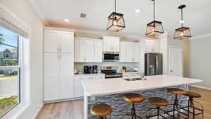 Una cocina moderna con armarios blancos, una isla grande con taburetes e iluminación colgante.
