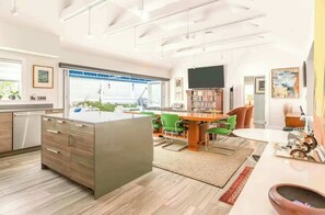 Une cuisine moderne avec un îlot central, un coin repas avec des chaises vertes et un téléviseur à écran plat fixé au mur.