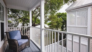 A covered porch with a wicker chair, white railings, and trees in the background.