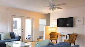 A living room with a sofa, a glass coffee table, a television, wicker chairs, and a ceiling fan.