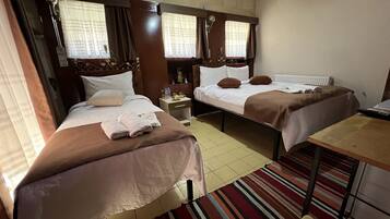 Quarto de hotel com duas camas de solteiro, uma mesinha, um criado-mudo e uma janela com cortinas.