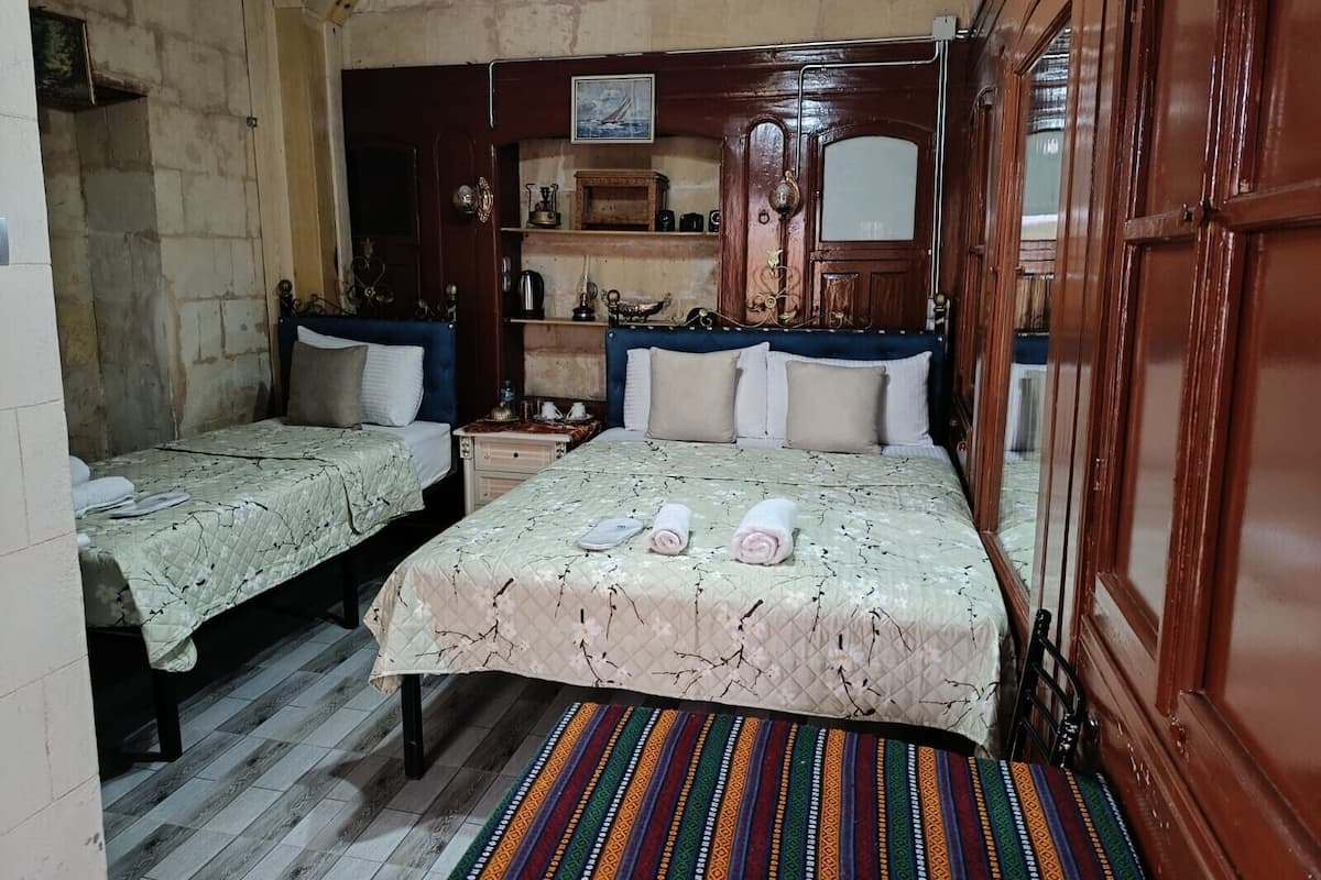 Ein Zimmer mit zwei Betten, einem Holzschrank, einem Regal mit Dekoration und einem farbenfrohen Streifen Teppich.
