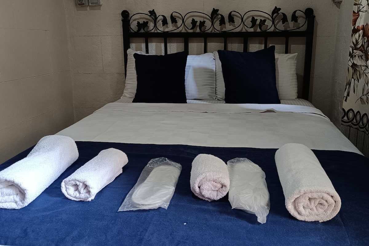Ein Bett mit blauer Bettdecke, weißen Kissen und aufgerollten Handtüchern.