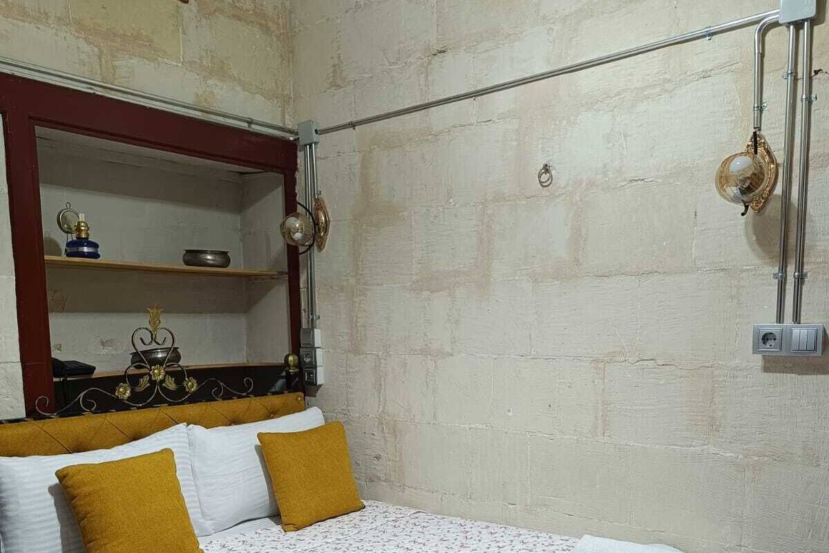 Ein Einzelbett mit floralem Überwurf, zwei senfgelbe Kissen und gerollte weiße Handtücher auf dem Bett.