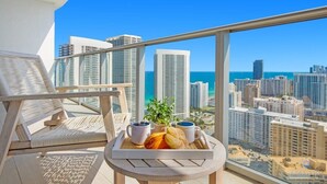 Un balcon avec une table préparée pour le petit-déjeuner, offrant une vue sur le paysage urbain et la mer.