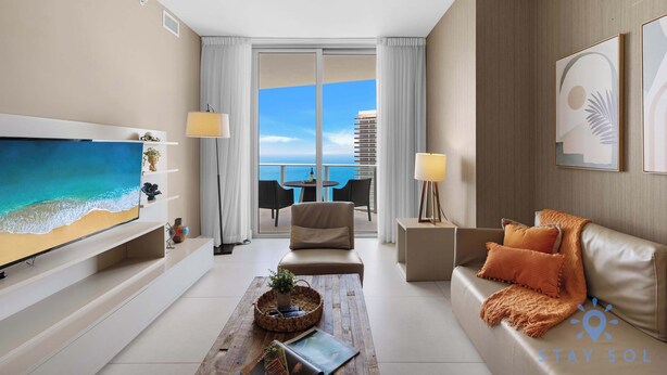 Ein modernes Hotelzimmer mit großem Fernseher, einer Couch, einem Couchtisch und einem Balkon mit Meerblick.