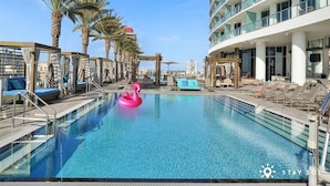 Ein Swimmingpool mit Liegestühlen und einem Flamingo-Schwimmpfaugel, umgeben von Palmen und einem modernen Gebäude.