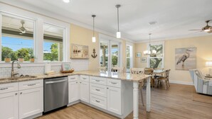 A kitchen with white cabinets, a dishwasher, a granite countertop, pendant lights, and a dining area with a table and chairs. - Seagrove Beach Home + Private Pool, & Bikes (Santa Rosa Beach)