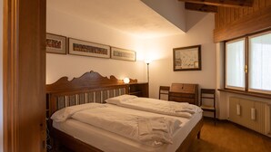 Une chambre à coucher avec un lit en bois, une table de chevet, une chaise et une fenêtre avec des stores.