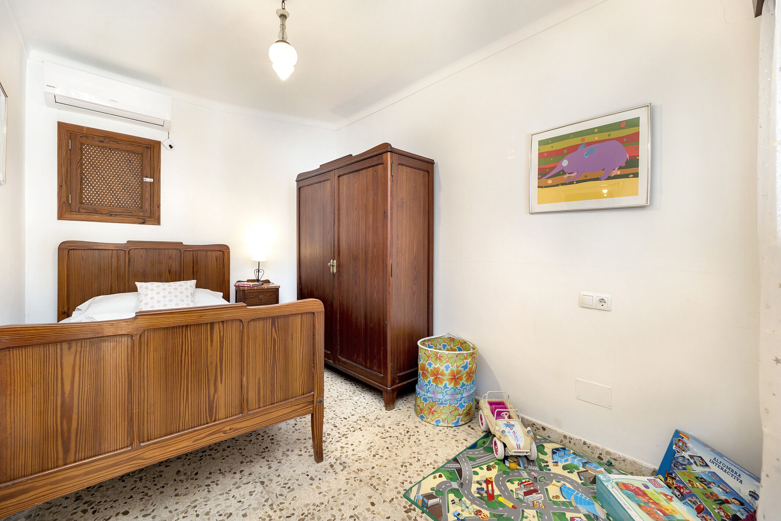Ein Schlafzimmer mit einem hölzernen Bett, einem Kleiderschrank, einem Mülleimer und Kinderspielzeug.