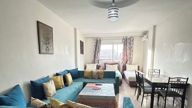 A living room with a teal sofa, a coffee table, a dining table with chairs, and a chandelier. - Family apartment 07 (Marrakech)