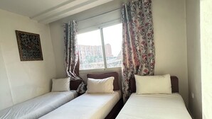 A room with two single beds, a sofa, a window with curtains, and an air conditioning unit. - Family apartment 07 (Marrakech)