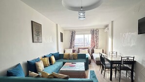 A living room with a teal sofa, a coffee table, and a dining area with a table and chairs. - Family apartment 07 (Marrakech)