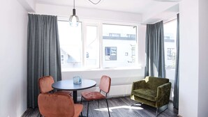 A modern room with a round table, two chairs, a green armchair, and a large window with curtains. - Svala Downtown Large Studio (Reykjavík)