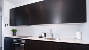 A modern kitchen with dark cabinetry, a stainless steel sink, and a built-in oven. - Svala Downtown Large Studio (Reykjavík)