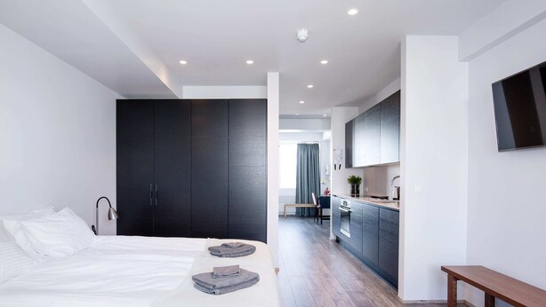A modern bedroom with a large bed, a dark wardrobe, and a small bench. - Svala Downtown Large Studio (Reykjavík)
