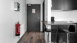 A modern kitchen with a dark door, a fire extinguisher, and two bar stools. - Svala Downtown Studio (Reykjavík)