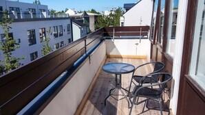 Un balcon doté d’un plancher en bois, de deux chaises en métal et d’une petite table ronde.
