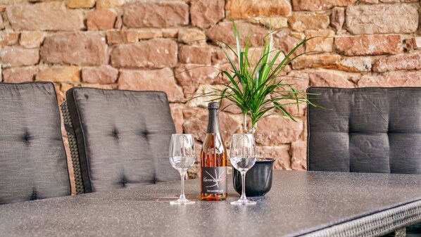 Een tafel met een fles en twee glaasjes, voor een bakstenen muur.
