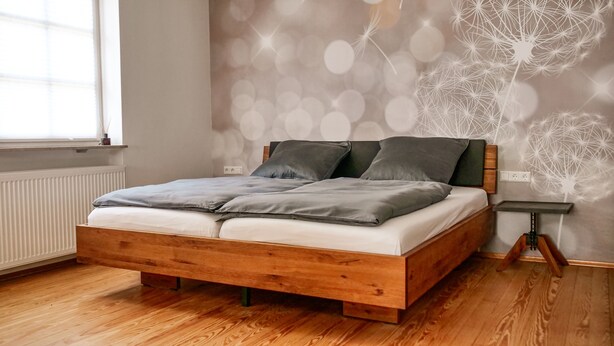 A wooden bed with grey bedding in a room with a dandelion-patterned wall.