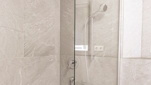 A walk-in shower with a glass door, a white shower seat, and a handheld showerhead.