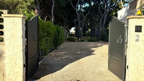 Un camino de grava que conduce a una entrada con puerta, con letreros que dicen 'Villa' y 'Edoardo', rodeado de árboles.